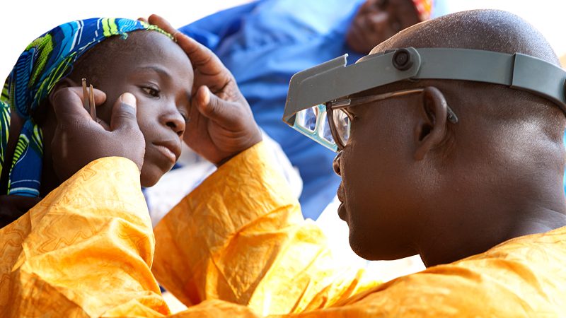 Dr. performs an eye exam on a young girl.